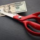 Red scissors cut money on black background. Financial concept